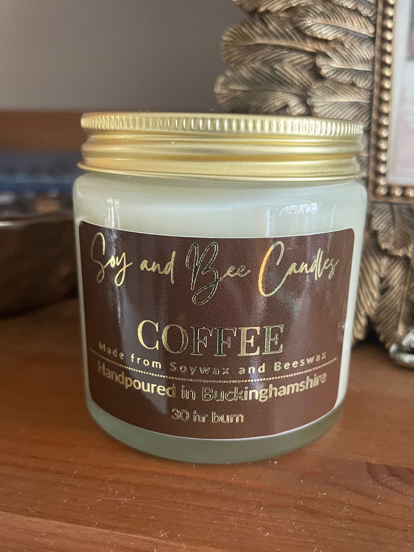 Jar of coffee candle on a wooden surface with decorative frame in the background