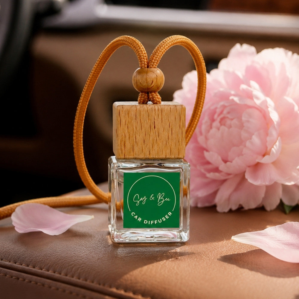Car diffuser with wooden top and green label next to pink flowers on a brown surface