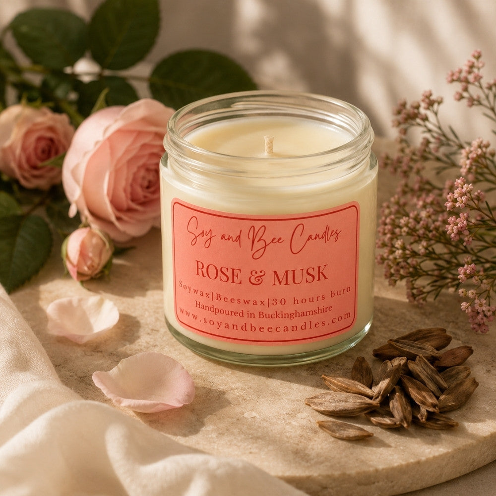 Candle jar labeled 'Rose & Musk' surrounded by flowers and petals on a neutral background